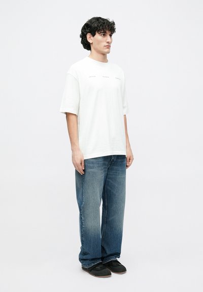 White cotton T-shirt with short sleeves and a loose fit, paired with blue denim jeans. Simple design with no visible patterns or graphics.