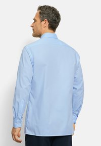 Camicia azzurra chiara con colletto button-down, maniche lunghe e una texture liscia; la vista posteriore rivela una vestibilità su misura.