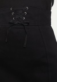 Falda de mezclilla negra con cintura alta y detalle de cordones de ojal, y una textura suave. El diseño incluye costuras planas y sin bolsillos visibles.