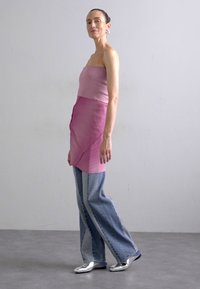 Trägerspitze pinkes Oberteil aus strukturiertem Stoff mit einem drapierten Design; kombiniert mit hellblauen weit geschnittenen Jeans und glänzenden silbernen Schuhen.