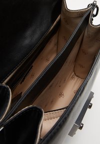 Czarna skórzana torebka z beżowym wnętrzem, wyposażona w dwie przegrody i markową podszewkę. Zawiera kieszeń na zamek i gładką fakturę.