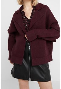 Bordeaux oversized kofta med slagkrage, texturerad tyg och sänkt axel, tillsammans med en svart kjol med dragkedja fram.