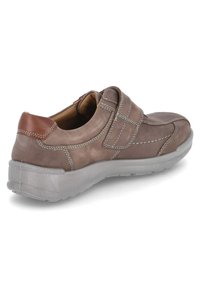 Brown leather sneaker with a Velcro strap, contrasting beige stitching, and a transparent rubber sole. Rounded toe and cushioned interior.