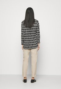 Blusa a maniche lunghe con motivo bianco e nero, abbinata a pantaloni beige chiaro e scarpe nere, vista da dietro.