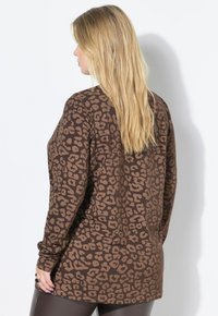 Chemise marron à manches longues avec un motif léopard noir, en tissu doux, coupe décontractée et col rond, portée avec des leggings foncés.