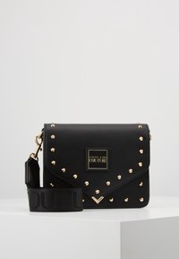 Borsa a tracolla nera in ecopelle con borchie dorate, pattina pieghevole, placca con logo e tracolla regolabile con dettagli testurizzati.