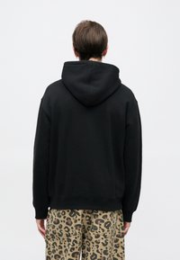 Μαύρο φούτερ με κουκούλα, άνετη εφαρμογή και ελαστικές μανσέτες, φορεμένο με μπεζ παντελόνι με μοτίβο λεοπάρδαλης.