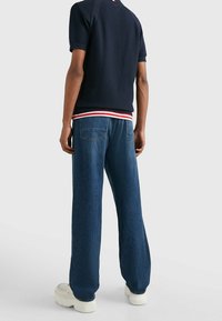 Marinblå texturerad kortärmad skjorta med röd och vit randig krage, tillsammans med vida blå denimbyxor och vita plattformssneakers.