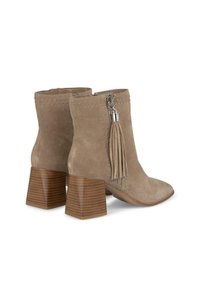 Botas de ante beige hasta el tobillo con punta afilada, tachuelas plateadas, detalle de borlas y un tacón de madera apilado. Cierre con cremallera en la parte posterior.