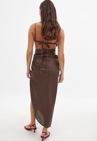 Sukně maxi z čokoládově hnědého lnu s uzavíráním na zadní straně, nastavitelné ramínka a boční rozparek. Má strukturovanou povrchovou úpravu.