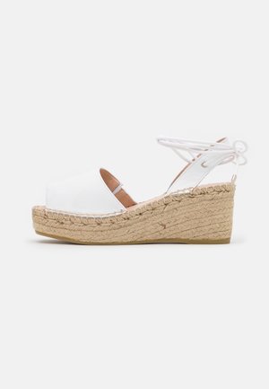 Sandale compensée en cuir blanc avec un design à bout ouvert, plateforme en jute et brides croisées. Présente une semelle texturée et des détails cousus.