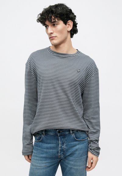 Γκρι και λευκό ριγέ μπλουζάκι με μακριά μανίκια, στρογγυλή λαιμόκοψη και άνετη εφαρμογή. Φέρει μικρό λογότυπο στο στήθος. Συνδυάζεται με ανοιχτόχρωμα τζιν.