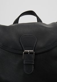 Czarna skórzana torba z górnym uchwytem i przednią klapą zabezpieczoną srebrnym metalowym zatrzaskiem.