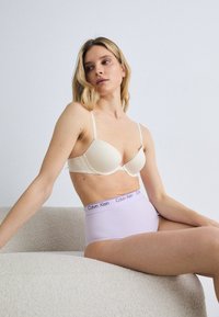 Beige padded bra with adjustable straps paired with high-waisted light purple underwear featuring a white Calvin Klein logo on the waistband.