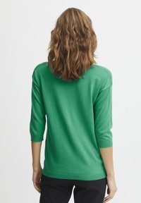 Zeleno, lahko, pleteno pulover s tremi četrtinskimi rokavi, sproščenim krojem ter rebrastim robom in manšetami. Gladka tekstura in enotna barva.