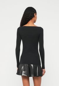 Μαύρο μακρυμάνικο τοπ με φαρδιά λαιμόκοψη, συνδυασμένο με πιετέ, γυαλιστερή μαύρη μίνι φούστα. Λεία υφή, εφαρμοστό σχέδιο.