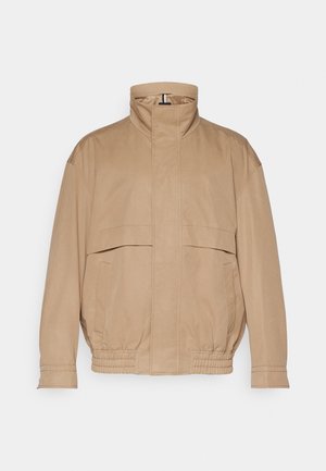 Veste légère de couleur marron clair faite d'un tissu doux. Comprend un col haut, deux poches avant, un ourlet élastiqué et des détails aux poignets.