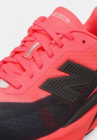 Chaussure de sport rose vif avec un dessus texturé, des accents noirs, un grand logo noir et des détails réfléchissants sur les lacets.