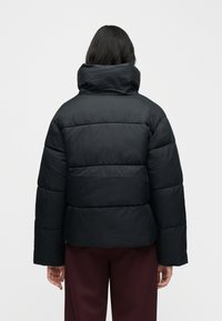 Čierna vetrovka s vysokým golierom, prešívaným dizajnom a širokými rukávmi. Hladká textúra s horizontálne prešívanými panelmi.