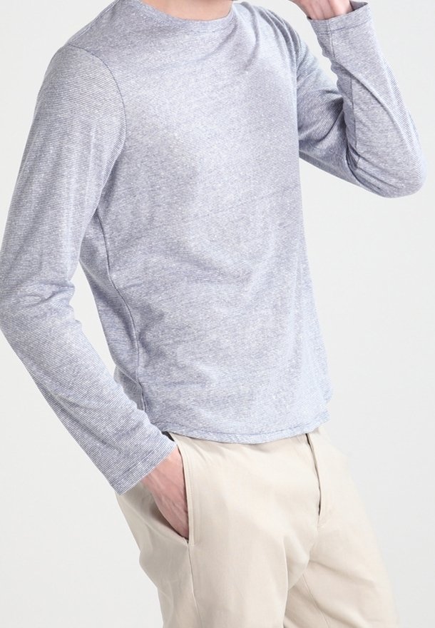 Chemise à manches longues et col rond de couleur gris clair, fabriquée en tissu doux avec une texture subtile. Elle présente un ourlet arrondi et des manches ajustées.