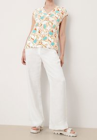 Haut à manches courtes avec un col en V, présentant un motif floral bleu et orange sur un fond crème. Associé à un pantalon large en lin blanc.