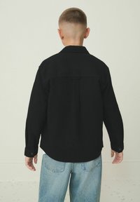 Schwarzes Hemd mit langen Ärmeln, geradem Schnitt und Rückenpasse, kombiniert mit hellblauen Jeans.