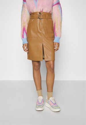 Osoba ubrana w beżową skórzaną spódnicę z przednim rozcięciem i paskiem, wielokolorowy pastelowy sweter, beżowe skarpetki oraz kolorowe dzianinowe sneakersy na platformie.