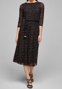 Vestido negro con mangas transparentes de tres cuartos, tela texturizada con un patrón geométrico y una cintura ceñida con un cinturón a juego.