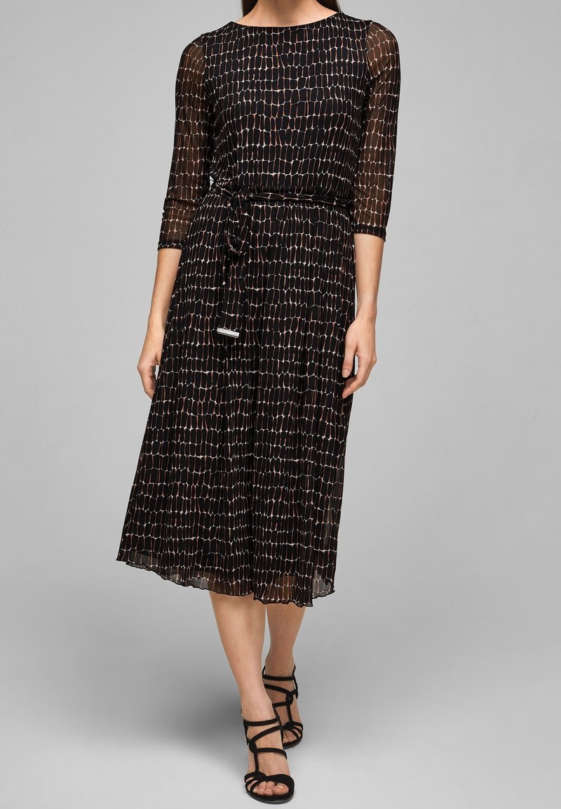 Vestido negro con mangas transparentes de tres cuartos, tela texturizada con un patrón geométrico y una cintura ceñida con un cinturón a juego.