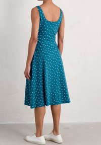 Teal klänning med vita prickar, ärmlös design, lätt utsvängd kjol, gjord av mjukt tyg, matchad med vita sneakers.