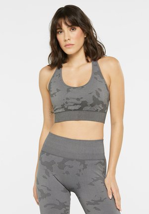 Sports bra in grey with a camouflage pattern, featuring a scoop neckline and wide underband. Fabric appears stretchy and smooth.