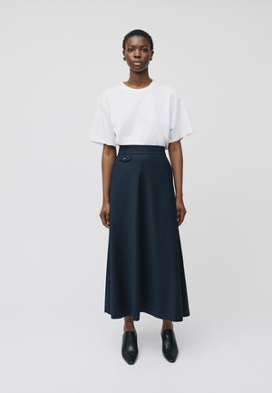 Camiseta blanca de manga corta combinada con una falda larga navy de cintura alta con un detalle de botones en el lado; la modelo lleva unos zuecos negros.
