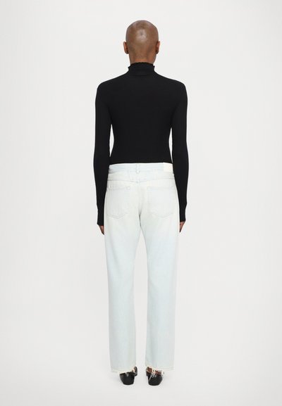 Polo de cuello alto negro de manga larga combinado con unos vaqueros de tiro alto azul claro, con dobladillos desflecados y una etiqueta de marca sutil en la parte posterior.