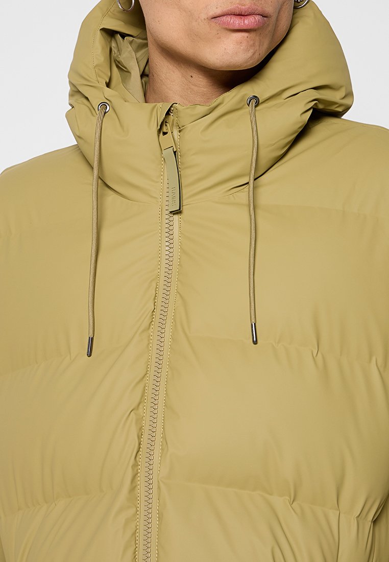 Gequiltde olijfgroene pufferjack met hoge kraag, ritssluiting en verstelbare trekkoordkap. Glad textuur en minimalistisch ontwerp.