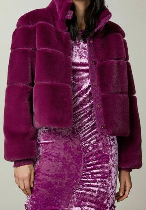 Vrouw die een paarse nepbont pufferjas draagt over een geplooide jurk van geplet fluweel in bijpassende paarse tinten.