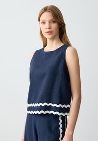Navyblaues, ärmelloses Oberteil aus einem Leinen-Mix mit gewelltem, weißen Saum. Weiche Textur, lässige Passform und runder Ausschnitt.