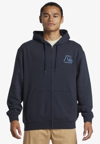 Námornícky zipsový svetre vyrobený z bavlnenej zmesi, s predným vreckom typu kangaroo, kapucňou so šnúrkami a svetlomodrým logom na hrudi.