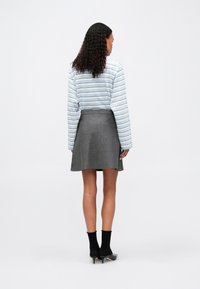Helles blau gestreiftes Langarmhemd, kombiniert mit einem grauen, schwingenden Rock. Das Outfit umfasst schwarze Socken und spitze schwarze Absätze, die eine glatte Textur zur Schau stellen.