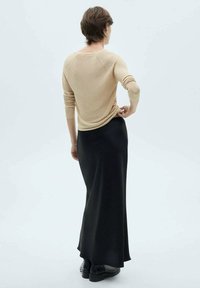 Beige Strickpullover mit langen Ärmeln, kombiniert mit einem schwarzen Maxirock. Das Outfit ist schlicht, mit weichen Texturen und einer lockeren Passform.