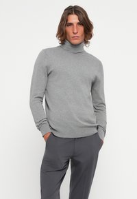 Siv turtleneck pulover iz mehke pletenine, ki ima dolge rokave in rebraste manšete, v kombinaciji s sivimi hlačami.