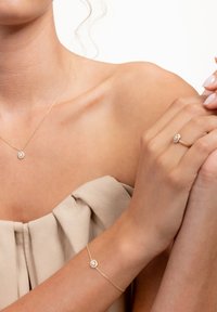 Gold chain necklace and bracelet, both featuring oval, gem-like accents. Smooth skin texture, soft beige clothing fabric draping.