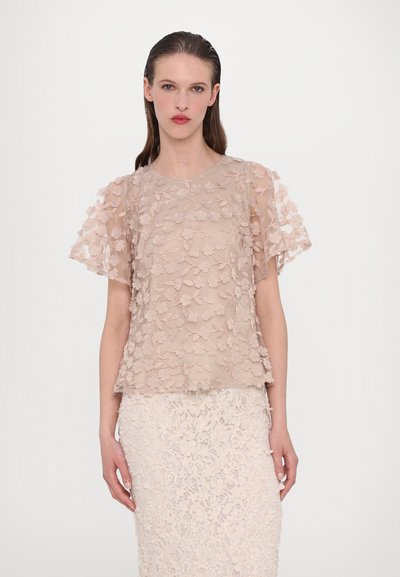 Transparante, beige top met bloemapplicé ontwerp, korte gerimpelde mouwen en een rechte snit. Draagt met een bijpassende kanten rok.