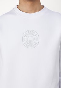 Sweatshirt blanc avec un logo en relief rond affichant "SUPER BOWL LVIII LAS VEGAS" et un design de casque de football au centre.