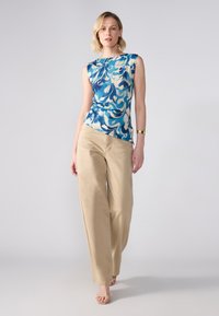 Top fără mâneci cu un model abstract albastru și crem, asortat cu pantaloni evazați bej. Material neted și croială lejeră, accentuată de o brățară.