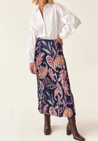 Blusa blanca de botones con mangas abullonadas combinada con una falda plisada de color azul marino con patrones florales y de paisley coloridos. Botas de tacón marrones.