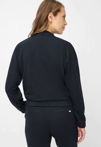 Schwarzer Pullover mit langen Ärmeln, hohem Kragen und elastischem Bund. Der Stoff wirkt weich mit einer glatten Textur und zeigt keine sichtbaren Muster.