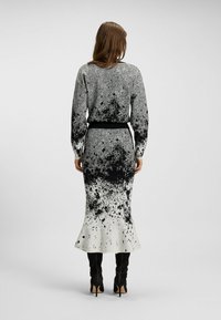 Schwarz-weißes Kleid mit einem Spritzmuster, das ein tailliertes Oberteil, einen ausgestellt Saum und eine Fischgrätenstruktur an den Ärmeln aufweist.