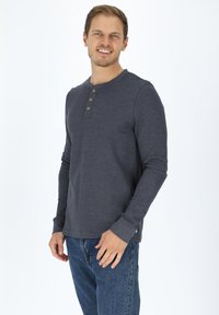 Mörkgrå långärmad henley-t-shirt i lätt tyg med tre träknappar vid halsen, i kombination med blå jeans.