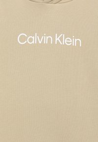 Béžová mikina s hladkou textúrou a bielym logom "Calvin Klein" na hrudi. Klasický dizajn s kapucňou.
