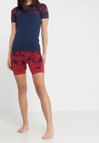 Mörkblå kortärmad aktiv topp med röda mönstrade shorts. Materialet är stretchigt, med en åtsittande design som har ett blommönster på shortsen.
